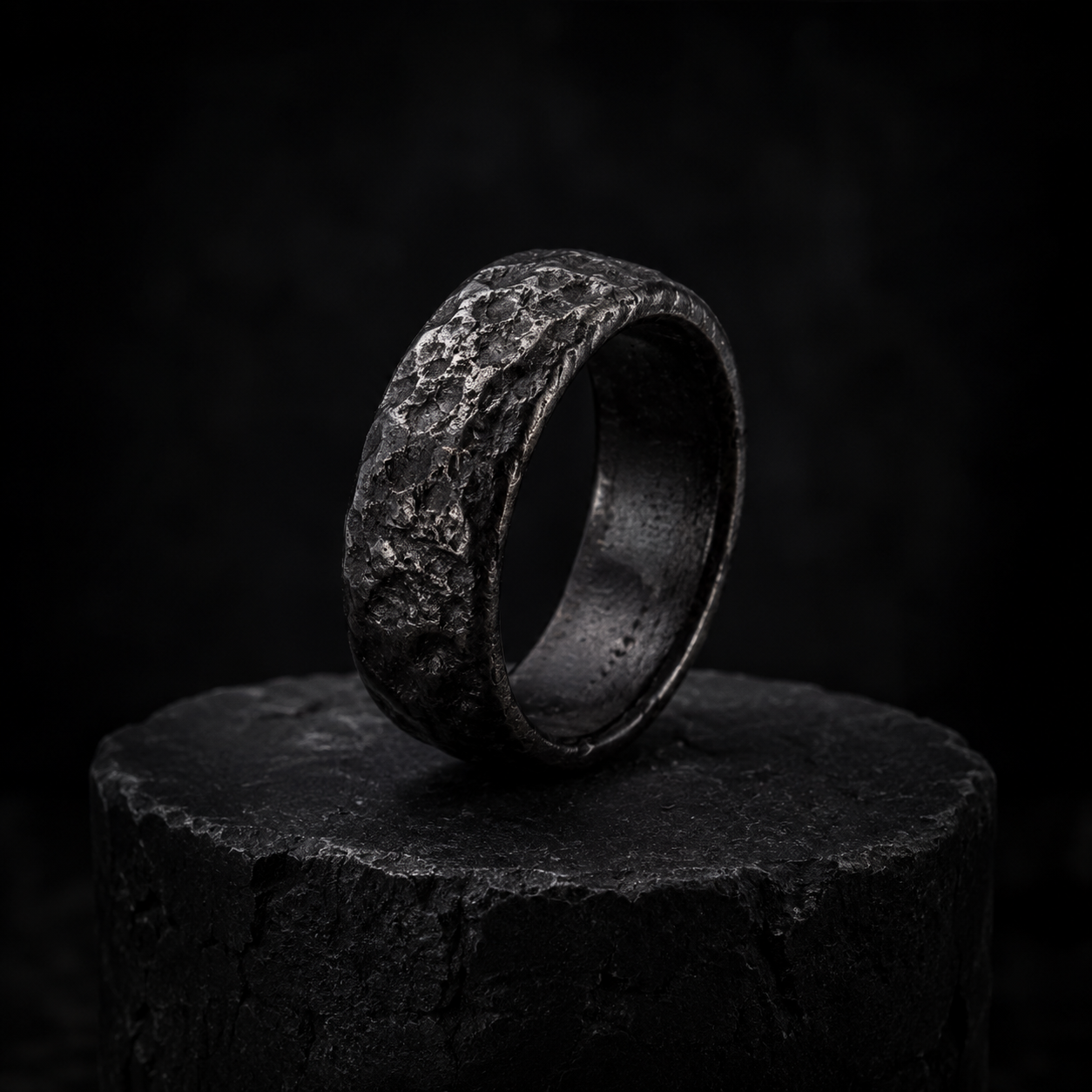 A rough black meteor-iron ring on a dark stone plinth